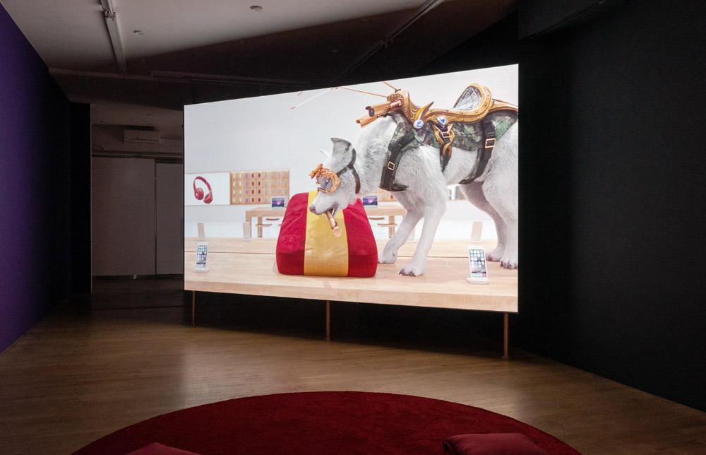 A dark room with a large screen at the front, showing a 3D animated scene of a grand, ornate interior with a pack of wolves prowling around. The scene is illuminated by the light coming from the screen, and the sound of the wolves' howls fills the room.